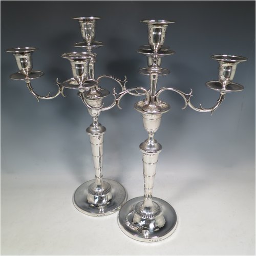An Antique Georgian / Victorian Sterling Silver pair of candelabra in a Neoclassical style, having removable arms with three lights, fluted and reed-banded columns with round bases, cast scroll-shaped arms, capitals with reeded decoration, removable nozzles with drip pans, and reed-edged borders. The candelabra bases are made by Matthew Boulton of Birmingham in 1795, whilst the branches are made by James Garrard of London in 1883. The dimensions of this fine hand-made pair of silver candelabra are height 41.5 cms (16.3 inches), and spread across arms 31.5 cms (12.3 inches). Please note that these are crested on the bases and nozzles.