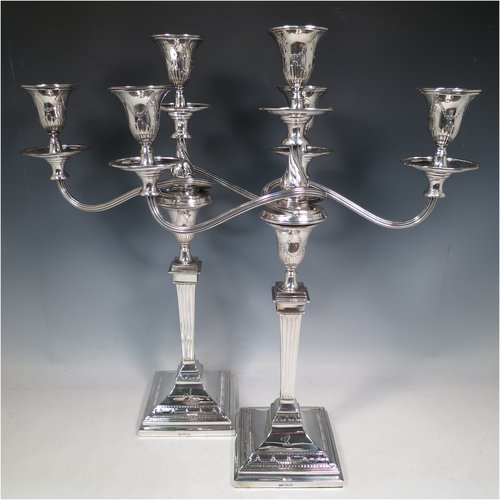 An Antique Edwardian Sterling Silver pair of candelabra in a Neoclassical style, having removable arms with three lights, fluted columns with stepped square bases, double swirl reeded arms, capitals with swags of flowers, removable nozzles with drip pans, and reed-edged borders. Made by George Hancock of London in 1903. The dimensions of this fine hand-made pair of silver candelabra are height 49 cms (19.25 inches), and spread across arms 37 cms (14.5 inches). Please note that these are crested on the bases.
