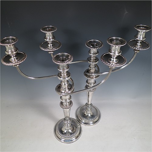 An Antique Georgian Old Sheffield Silver Plated pair of candelabra in a very elegant Regency style, having removable arms with three lights, with plain round baluster columns and bases, and plain reeded double swirl arms, removable nozzles with drip pans, and gadroon edged borders. Made in ca. 1815. The dimensions of this fine hand-made pair of Old Sheffield three-light candelabra are height 49 cms (19.25 inches), and spread across arms 39.5 cms (15.5 inches). Please note that the bases are crested.
