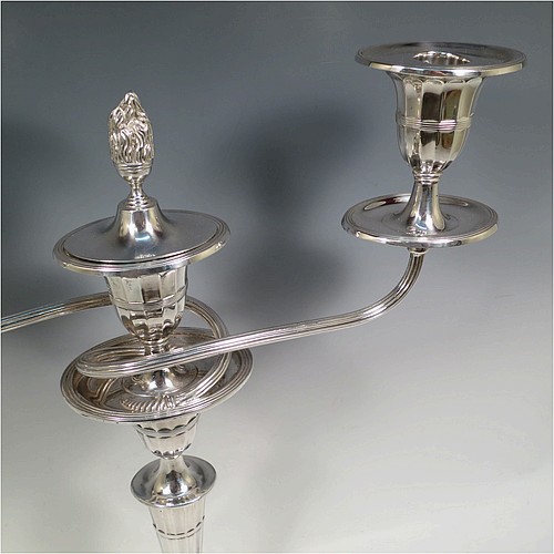 A very pretty pair of Antique Sterling Silver candelabra in a Neoclassical style, having removable arms with three lights, fluted columns with oval bases, double swirl and reeded arms, capitals with fluted and reeded decoration, removable nozzles with drip pans and a central flame extinguisher, and reed-edged borders. Made by William Hutton and Sons of Sheffield in 1913. The dimensions of this fine hand-made pair of antique silver candelabra are height 43 cms (17 inches), and spread across arms 34 cms (13.3 inches).