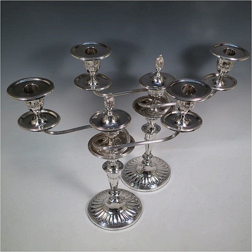 A very pretty pair of Antique Sterling Silver candelabra in a Neoclassical style, having removable arms with three lights, fluted columns with oval bases, double swirl and reeded arms, capitals with fluted and reeded decoration, removable nozzles with drip pans and a central flame extinguisher, and reed-edged borders. Made by William Hutton and Sons of Sheffield in 1913. The dimensions of this fine hand-made pair of antique silver candelabra are height 43 cms (17 inches), and spread across arms 34 cms (13.3 inches).