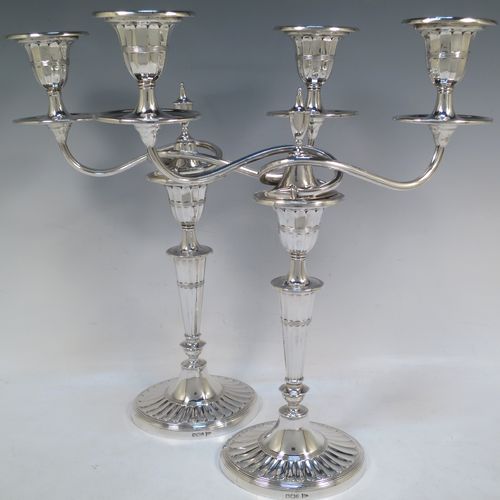 A very pretty pair of Antique Victorian Sterling Silver candelabra in a Neoclassical style with hand-chased fluting and reeded decoration, having removable arms with two lights, with oval bases, reeded scroll-shaped arms, capitals with removable nozzles and drip pans, and reed-edged borders. Made by Walker and Hall of Sheffield in 1901. The dimensions of this fine hand-made pair of antique silver candelabra are height 33 cms (13 inches), and spread across arms 27 cms (10.5 inches).  