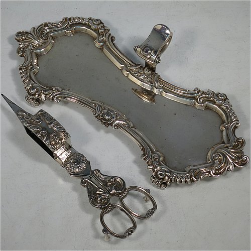 An Antique Georgian Old Sheffield Plated candle scissor snuffer stand and candle scissor snuffer, the stand having an applied floral & scroll border with a cast scroll handle and sitting on four cast scroll feet, the scissor snuffer with matching decoration and all in original working condition. Made in ca. 1820. The dimensions of this fine hand-made antique Old Sheffield Plated snuffer stand and scissors are length 24 cms (9.5 inches), height (inc. handle) 5 cms (2 inches), and width (inc. handle) 11 cms (4.25 inches),