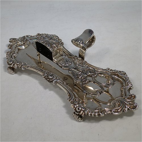 An Antique Georgian Old Sheffield Plated candle scissor snuffer stand and candle scissor snuffer, the stand having an applied floral & scroll border with a cast scroll handle and sitting on four cast scroll feet, the scissor snuffer with matching decoration and all in original working condition. Made in ca. 1820. The dimensions of this fine hand-made antique Old Sheffield Plated snuffer stand and scissors are length 24 cms (9.5 inches), height (inc. handle) 5 cms (2 inches), and width (inc. handle) 11 cms (4.25 inches),