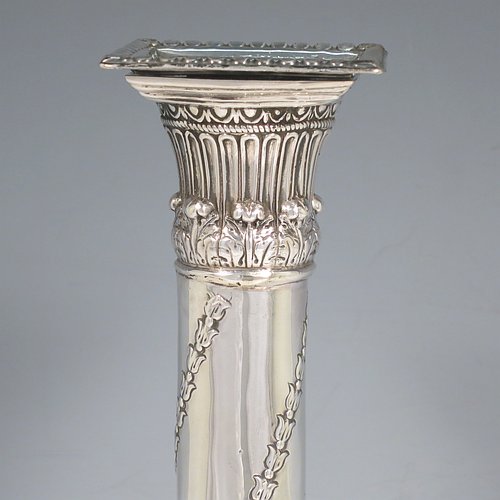 An Antique Georgian Sterling Silver pair of table candlesticks, in a Neoclassical style having square bases with hand-chased floral swags and rams heads, the columns with swirled garlands of flowers, scroll capitals with anthemion leaves, and removable nozzles with bead borders. Made by John Hoyland & Co., of Sheffield in 1777. The dimensions of theses fine antique silver candlesticks are height 28.5 cms (11.25 inches), bases 12.5 cms (5 inches) square.   