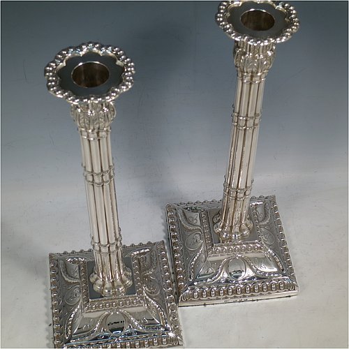 An Antique Georgian Sterling Silver pair of table candlesticks, in a Neoclassical style having square bases with bead borders, hand-chased floral swags and male head motifs, the columns in a bound palm-tree style with frond capitals, and removable nozzles. Made by John Cox of London in 1771. The dimensions of these fine antique silver candlesticks are height 32 cms (12.5 inches), bases 12.5 cms (5 inches) square. Please note that these candlesticks are crested.
