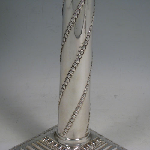 Antique Victorian sterling silver pair of table candlesticks, in a Neoclassical style having square stepped bases with hand-chased floral work, the columns with swirled garlands of flowers, scroll capitals with swags, and removable nozzles with gadroon borders. Made by William Hutton of London in 1901. Height 27.5 cms (10.75 inches), bases 11 cms (4.25 inches) square.