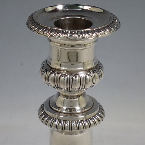 An Antique Georgian Sterling Silver handsome pair of Regency style candlesticks, having round baluster bodies, with removable nozzles, and sitting on round bases, all with hand-chased melon-fluted decoration and applied gadroon borders. Made by John Roberts & Co., of Sheffield in 1811. The dimensions of these fine hand-made antique silver table candlesticks are height 19.5 cms (7.75 inches), and the bases are 12 cms (4.75 inches) in diameter. Please note that these candlesticks are crested with the Latin motto Ne Vile Fano for the Earls of Westmorland.