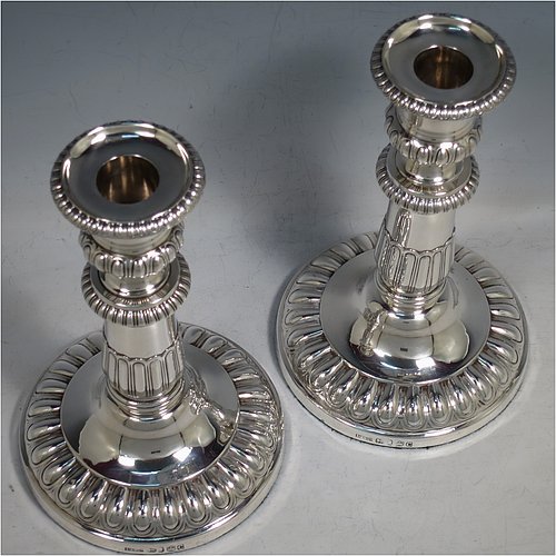 An Antique Georgian Sterling Silver handsome pair of Regency style candlesticks, having round baluster bodies, with removable nozzles, and sitting on round bases, all with hand-chased melon-fluted decoration and applied gadroon borders. Made by John Roberts & Co., of Sheffield in 1811. The dimensions of these fine hand-made antique silver table candlesticks are height 19.5 cms (7.75 inches), and the bases are 12 cms (4.75 inches) in diameter. Please note that these candlesticks are crested with the Latin motto Ne Vile Fano for the Earls of Westmorland.