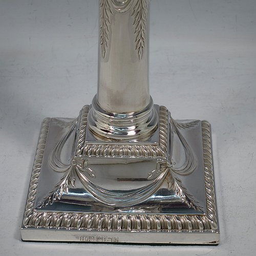 An Antique Edwardian Sterling Silver pair of candlesticks, in a Neoclassical Corinthian style with square bases and round straight-sided columns, having applied gadroon borders, hand-chased bows with swag decoration, and removable nozzles. Made by Henry Wilkinson of Sheffield in 1902. The dimensions of this fine pair of hand-made antique silver candlesticks are height 19 cms (7.5 inches), and the bases are 10 cms (4 inches) square.