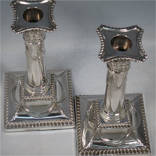 An Antique Edwardian Sterling Silver pair of candlesticks, in a Neoclassical Corinthian style with square bases and round straight-sided columns, having applied gadroon borders, hand-chased bows with swag decoration, and removable nozzles. Made by Henry Wilkinson of Sheffield in 1902. The dimensions of this fine pair of hand-made antique silver candlesticks are height 19 cms (7.5 inches), and the bases are 10 cms (4 inches) square.