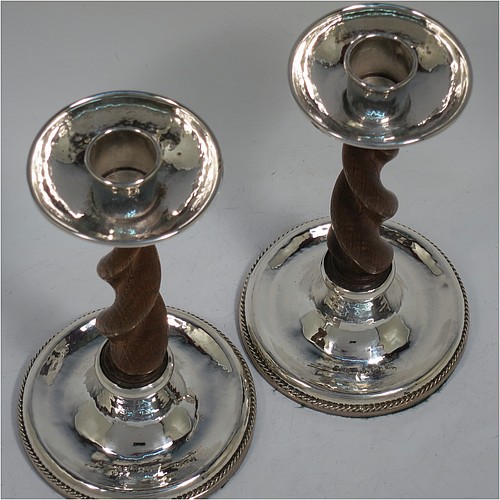 A very unusual and pretty Sterling Silver pair of Arts and Crafts candlesticks, having round bases with a hand-hammered finish and applied rope-twist lower borders, with hand-carved wooden swirl columns, and round capitals with deep drip pans. Made by A. E. Jones of Birmingham in 1920. The dimensions of these fine hand-made Arts and Crafts silver candlesticks are height 17 cms (6.75 inches), and diameter at base 10 cms (4 inches).