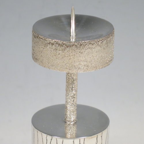 A Sterling Silver pair of candlesticks in a Modernistic style, having cylindrical bodies with hand-chased tree-bark decoration, together with capitals and candle spikes with an unusual stippled finish. Made by Michael Bensted of London in 1975. The dimensions of these fine hand-made pair of silver table candlesticks are height 19 cms (7.5 inches), diameter 4 cms (1.5 inches), and they weigh a total of approx. 437g (14.1 troy ounces). Please note that these candlesticks are not filled.