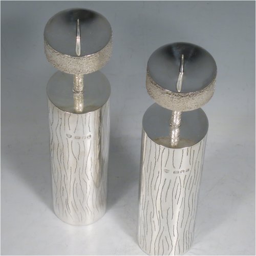 A Sterling Silver pair of candlesticks in a Modernistic style, having cylindrical bodies with hand-chased tree-bark decoration, together with capitals and candle spikes with an unusual stippled finish. Made by Michael Bensted of London in 1975. The dimensions of these fine hand-made pair of silver table candlesticks are height 19 cms (7.5 inches), diameter 4 cms (1.5 inches), and they weigh a total of approx. 437g (14.1 troy ounces). Please note that these candlesticks are not filled.