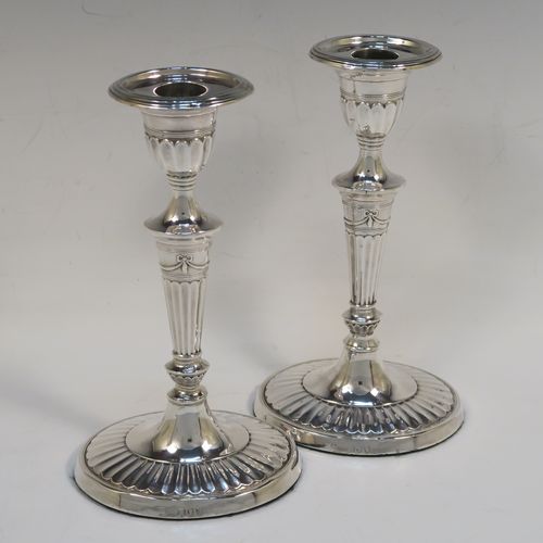 A very pretty pair of Antique Victorian Sterling Silver candlesticks, having Neoclassical style oval shaped bodies, with hand-chased fluted decoration, reeded borders, bows and swags, and removable nozzles. These beautiful antique silver candlesticks were made by Holland, Aldwinckle, and Slater of London in 1894. The dimensions of these fine hand-made pair of antique silver table candlesticks are height 18.5 cms (7.25 inches), length at base 10 cms (4 inches), and width at base 7.5 cms (3 inches).  