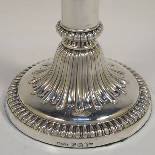 A very handsome Antique Georgian Sterling Silver handsome pair of Regency style candlesticks, having round baluster bodies, with removable nozzles, and sitting on round bases, all with hand-chased melon-fluted decoration and applied gadroon borders. These elegant antique silver candlesticks were made by John and Thomas Settle of Sheffield in 1819. The dimensions of these fine hand-made antique silver table candlesticks are height 21 cms (8.25 inches), and the bases are 12.5 cms (5 inches) in diameter.