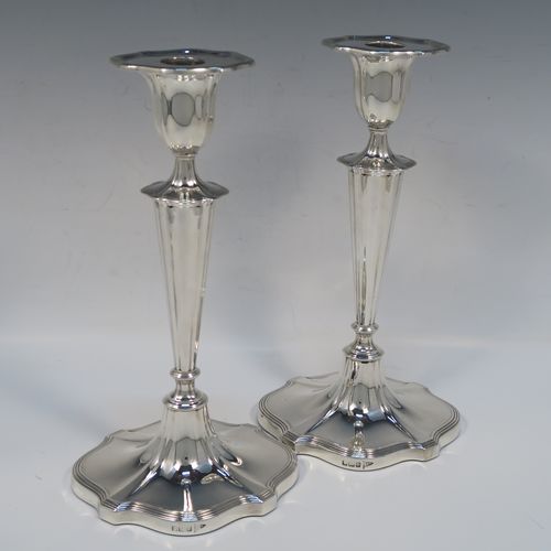 A very handsome pair of Antique Edwardian Sterling Silver candlesticks, having Neoclassical style oval shaped bodies, with hand-chased fluted decoration, reeded borders, and removable nozzles. These elegant silver candlesticks were made by Walker and Hall of Sheffield in 1909. The dimensions of this fine hand-made pair of antique silver table candlesticks are height 24 cms (9.5 inches), length at base 13 cms (5 inches), and width at base 10 cms (4 inches).   