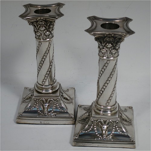 A very striking Antique Victorian Sterling Silver pair of candlesticks, in a Corinthian style with bead-edged borders, removable nozzles, columns with twisted bluebell garlands, and square bases with hand-chased swags of flowers and rams heads. Made by William Hutton of London in 1900. The dimensions of this fine pair of hand-made antique silver candlesticks are height 15 cms (6 inches), and the bases are 8 cms (3.25 inches) square.    