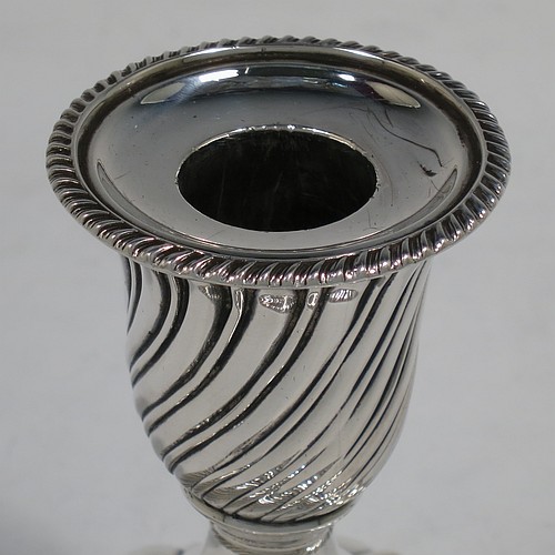 A very pretty Antique Victorian Sterling Silver pair of small candlesticks, having round bodies with hand-chased swirl-fluted decoration, and removable nozzles with applied gadroon borders. Made by Henry Holland of London in 1895. The dimensions of these fine hand-made antique silver candlesticks are height 10 cms (4 inches), and the bases are 9 cms (3.5 inches) in diameter.