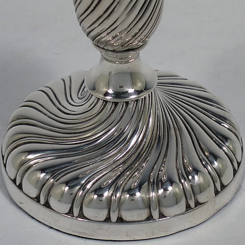 A very pretty Antique Victorian Sterling Silver pair of small candlesticks, having round bodies with hand-chased swirl-fluted decoration, and removable nozzles with applied gadroon borders. Made by Henry Holland of London in 1895. The dimensions of these fine hand-made antique silver candlesticks are height 10 cms (4 inches), and the bases are 9 cms (3.5 inches) in diameter.