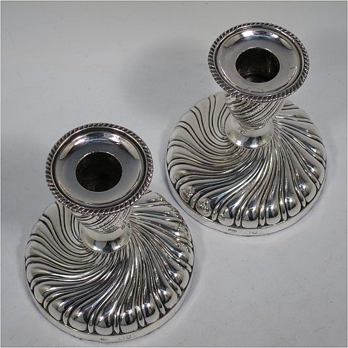 A very pretty Antique Victorian Sterling Silver pair of small candlesticks, having round bodies with hand-chased swirl-fluted decoration, and removable nozzles with applied gadroon borders. Made by Henry Holland of London in 1895. The dimensions of these fine hand-made antique silver candlesticks are height 10 cms (4 inches), and the bases are 9 cms (3.5 inches) in diameter.