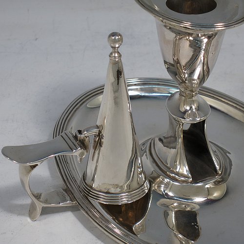 An Antique Georgian Sterling Silver chamber-stick, having an oval body, a plain scroll handle with thumb-piece, an original removable dunce-cap extinguisher, an original removable nozzle, and with applied reed-edged borders. Made by William Bennett of London in 1802. The dimensions of this fine hand-made antique silver chamberstick are width 16 cms (6.3 inches), depth 15 cms (6 inches), height 10 cms (4 inches), and it weighs approx. 319g (10.3 troy ounces).