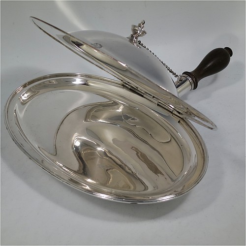 A very handsome Antique Georgian Sterling Silver cheese dish, having a very plain oval body with reeded borders, a cast urn-shaped finial, and a flat hidden hinge, attached to a hollow oval hot-water jacket base with removable oak wood-turned handle and a security chain to hold the lid at an angle to reflect heat from fire onto cheese. Made by John King of London in 1788. The dimensions of this fine hand-made antique silver cheese dish are length (inc. handle) 29 cms (11.5 inches), with 25.5 cms (10 inches), height 8 cms (3 inches), and it weighs approx. 850g (27 troy ounces). Please note that this item is crested.