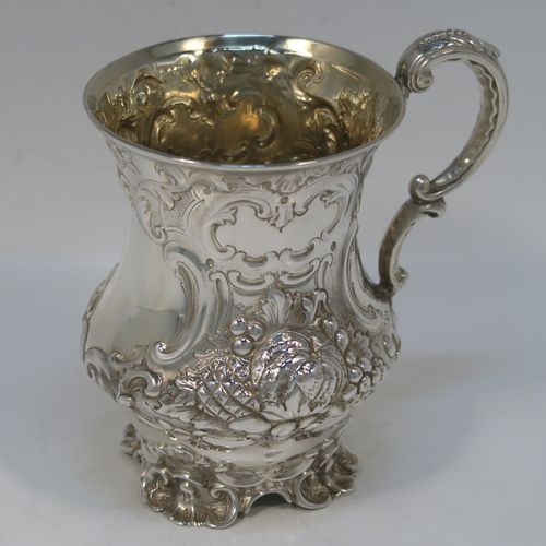 A very pretty Antique Victorian Sterling Silver christening mug, having a round bellied body with hand-chased floral and scroll-work decoration surrounding a vacant front cartouche, a cast scroll side-handle, a gold-gilt interior, and all sitting on four cast foliate feet. This beautiful antique silver christening mug was made by Martin Hall and Co., of Sheffield in 1856. The dimensions of this fine hand-made antique silver christening mug are height 11.5 cms (4.5 inches), diameter at lip 8 cms (3 inches), and it weighs approx. 163g (5.3 troy ounces).