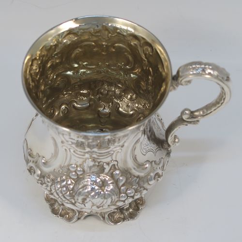 A very pretty Antique Victorian Sterling Silver christening mug, having a round bellied body with hand-chased floral and scroll-work decoration surrounding a vacant front cartouche, a cast scroll side-handle, a gold-gilt interior, and all sitting on four cast foliate feet. This beautiful antique silver christening mug was made by Martin Hall and Co., of Sheffield in 1856. The dimensions of this fine hand-made antique silver christening mug are height 11.5 cms (4.5 inches), diameter at lip 8 cms (3 inches), and it weighs approx. 163g (5.3 troy ounces).