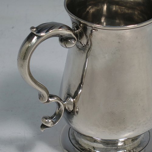 An Antique Georgian Sterling Silver christening mug, having a plain round bellied body, a scroll handle, and sitting on a collet foot. Made in London in 1774. The dimensions of this fine hand-made antique silver christening mug are height 9.5 cms (3.75 inches), diameter at top 6 cms (2.3 inches), and it weighs approx. 175g (5.6 troy ounces).