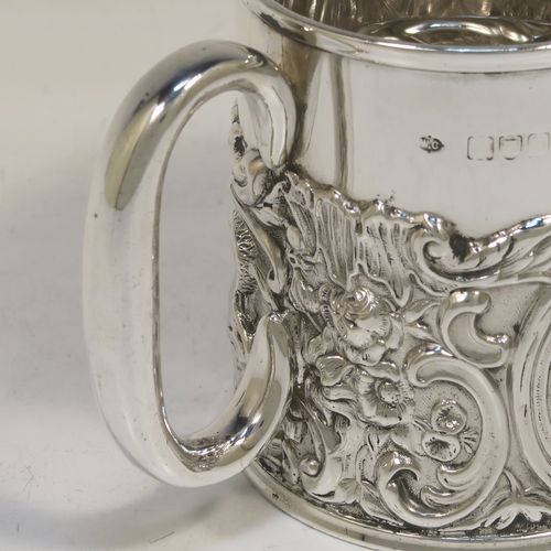 A pretty Antique Victorian Sterling Silver christening mug, having a round straight sided body with a reeded top border, a lower band of hand-chased scroll and floral decoration, a plain loop side-handle, and all sitting on a flat base. This beautiful antique silver christening mug was made by William Comyns of London in 1897. The dimensions of this fine hand-made antique silver christening mug are height 9 cms (3.5 inches), diameter at lip 7.5 cms (3 inches), and it weighs approx. 168g (5.4 troy ounces).