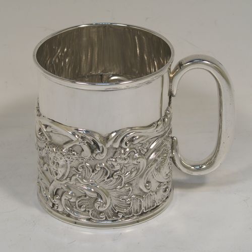 A pretty Antique Victorian Sterling Silver christening mug, having a round straight sided body with a reeded top border, a lower band of hand-chased scroll and floral decoration, a plain loop side-handle, and all sitting on a flat base. This beautiful antique silver christening mug was made by William Comyns of London in 1897. The dimensions of this fine hand-made antique silver christening mug are height 9 cms (3.5 inches), diameter at lip 7.5 cms (3 inches), and it weighs approx. 168g (5.4 troy ounces).