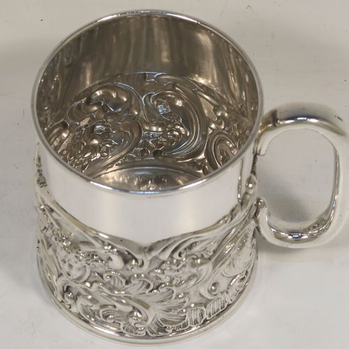 A pretty Antique Victorian Sterling Silver christening mug, having a round straight sided body with a reeded top border, a lower band of hand-chased scroll and floral decoration, a plain loop side-handle, and all sitting on a flat base. This beautiful antique silver christening mug was made by William Comyns of London in 1897. The dimensions of this fine hand-made antique silver christening mug are height 9 cms (3.5 inches), diameter at lip 7.5 cms (3 inches), and it weighs approx. 168g (5.4 troy ounces).