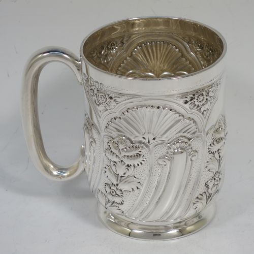 A very pretty Antique Victorian Sterling Silver christening mug, having a round straight-sided body with tucked under belly, all hand-chased with  floral and scroll-work decoration, a central vacant half-moon style cartouche, a plain loop handle, and all sitting on a collet foot. Made by George Maudsley Jackson of London in 1892. The dimensions of this fine hand-made antique silver christening mug are height 9.5 cms (3.75 inches), diameter at lip 7 cms (2.75 inches), and it weighs approx. 149g (4.8 troy ounces).   