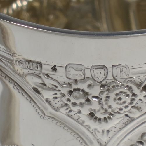 A very pretty Antique Victorian Sterling Silver christening mug, having a round straight-sided body with tucked under belly, all hand-chased with floral and scroll-work decoration, a central vacant half-moon style cartouche, a plain loop handle, and all sitting on a collet foot. Made by George Maudsley Jackson of London in 1892. The dimensions of this fine hand-made antique silver christening mug are height 9.5 cms (3.75 inches), diameter at lip 7 cms (2.75 inches), and it weighs approx. 149g (4.8 troy ounces).