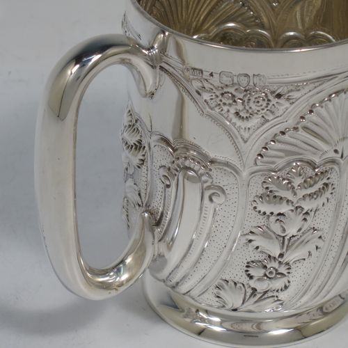 A very pretty Antique Victorian Sterling Silver christening mug, having a round straight-sided body with tucked under belly, all hand-chased with floral and scroll-work decoration, a central vacant half-moon style cartouche, a plain loop handle, and all sitting on a collet foot. Made by George Maudsley Jackson of London in 1892. The dimensions of this fine hand-made antique silver christening mug are height 9.5 cms (3.75 inches), diameter at lip 7 cms (2.75 inches), and it weighs approx. 149g (4.8 troy ounces).