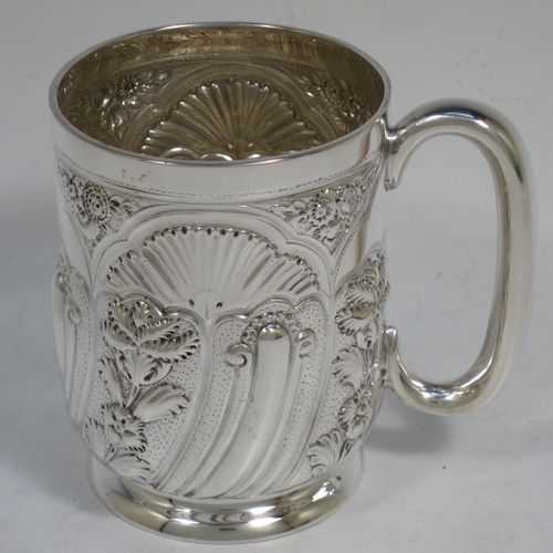 A very pretty Antique Victorian Sterling Silver christening mug, having a round straight-sided body with tucked under belly, all hand-chased with floral and scroll-work decoration, a central vacant half-moon style cartouche, a plain loop handle, and all sitting on a collet foot. Made by George Maudsley Jackson of London in 1892. The dimensions of this fine hand-made antique silver christening mug are height 9.5 cms (3.75 inches), diameter at lip 7 cms (2.75 inches), and it weighs approx. 149g (4.8 troy ounces).