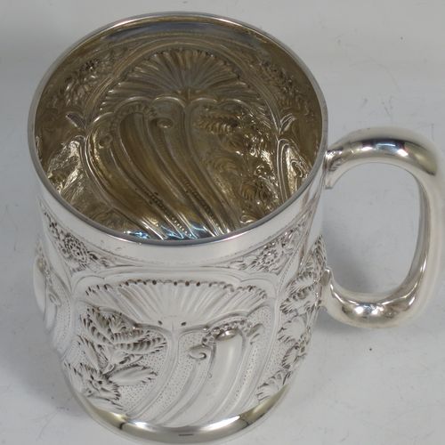 A very pretty Antique Victorian Sterling Silver christening mug, having a round straight-sided body with tucked under belly, all hand-chased with floral and scroll-work decoration, a central vacant half-moon style cartouche, a plain loop handle, and all sitting on a collet foot. Made by George Maudsley Jackson of London in 1892. The dimensions of this fine hand-made antique silver christening mug are height 9.5 cms (3.75 inches), diameter at lip 7 cms (2.75 inches), and it weighs approx. 149g (4.8 troy ounces).