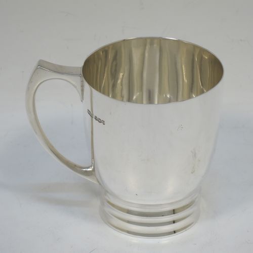 A very handsome Art Deco style Sterling Silver christening mug, having a plain round body with tapering sides, a scroll handle, and sitting on a pedestal foot with banded decoration. Made by James Dixon and Sons of Sheffield in 1938. The dimensions of this fine hand-made Art Deco silver christening mug are height 8 cms (3.25 inches), length 9 cms (3.5 inches), and it weighs approx. 165g (5.3 troy ounces).