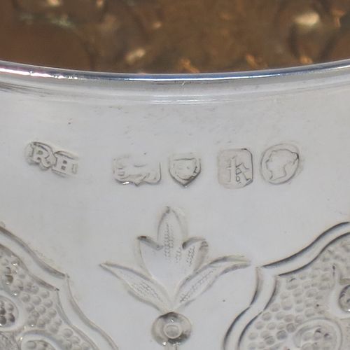 A very pretty Antique Victorian Sterling Silver christening mug, having a round body with straight tapering sides and tucked under belly, with hand-chased floral and scroll-work decoration surrounding four vacant lobed cartouches, a scroll loop handle, a gold-gilt interior, and all sitting on a pedestal foot. Made by Robert Hennell of London in 1865. The dimensions of this fine hand-made antique silver christening mug are height 10 cms (4 inches), diameter at lip 7 cms (2.75 inches), and it weighs approx. 130g (4.2 troy ounces).  