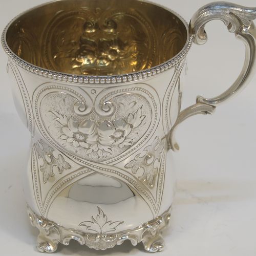 A very pretty Antique Victorian Sterling Silver christening mug, having a round bellied body with hand-chased floral and scroll-work decoration, an applied bead-edged top border, a cast scroll side-handle, a gold-gilt interior, and all sitting on four cast foliate feet. This beautiful antique silver christening mug was made by Elizabeth and John Eaton of London in 1862. The dimensions of this fine hand-made antique silver christening mug are height 10 cms (4 inches), diameter at lip 7.5 cms (3 inches), and it weighs approx. 130g (4.2 troy ounces).