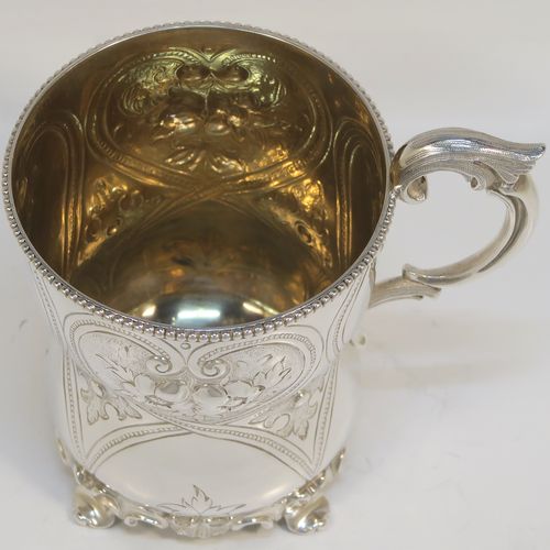 A very pretty Antique Victorian Sterling Silver christening mug, having a round bellied body with hand-chased floral and scroll-work decoration, an applied bead-edged top border, a cast scroll side-handle, a gold-gilt interior, and all sitting on four cast foliate feet. This beautiful antique silver christening mug was made by Elizabeth and John Eaton of London in 1862. The dimensions of this fine hand-made antique silver christening mug are height 10 cms (4 inches), diameter at lip 7.5 cms (3 inches), and it weighs approx. 130g (4.2 troy ounces).