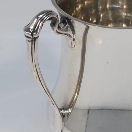 An unusual and very handsome Sterling Silver Tyg-style christening mug, having a plain round bellied body, with three scroll side-handles, and sitting on a pedestal foot. This elegant silver Tyg mug was made by the Atkins Brothers of Sheffield in 1927. The dimensions of this fine hand-made silver christening mug are height 9 cms (3.5 inches), diameter at top 6.5 cms (2.5 inches), and it weighs approx. 191g (6.2 troy ounces).