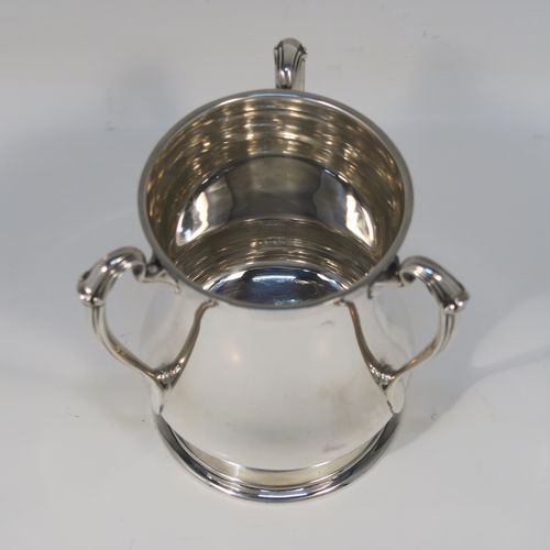 An unusual and very handsome Sterling Silver Tyg-style christening mug, having a plain round bellied body, with three scroll side-handles, and sitting on a pedestal foot. This elegant silver Tyg mug was made by the Atkins Brothers of Sheffield in 1927. The dimensions of this fine hand-made silver christening mug are height 9 cms (3.5 inches), diameter at top 6.5 cms (2.5 inches), and it weighs approx. 191g (6.2 troy ounces).