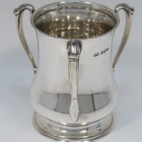 An unusual and very handsome Sterling Silver Tyg-style christening mug, having a plain round bellied body, with three scroll side-handles, and sitting on a pedestal foot. This elegant silver Tyg mug was made by the Atkins Brothers of Sheffield in 1927. The dimensions of this fine hand-made silver christening mug are height 9 cms (3.5 inches), diameter at top 6.5 cms (2.5 inches), and it weighs approx. 191g (6.2 troy ounces).