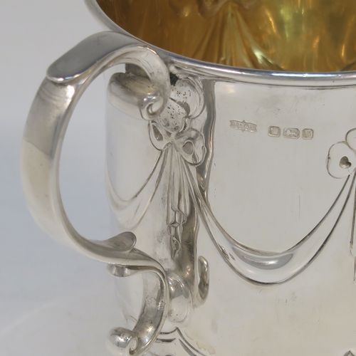 A very pretty Antique Edwardian Sterling Silver christening mug, having a round bellied body, with hand-chased ribbons, swags, and lotus leaf decoration, a cast scroll side-handle, a gold-gilt interior, and sitting on a pedestal foot. This beautiful antique silver christening mug was made by James Dixon and Sons of Sheffield in 1910. The dimensions of this fine hand-made antique silver christening mug are height 10 cms (4 inches), length 10 cms (4 inches), and it weighs approx. 151g (4.9 troy ounces).