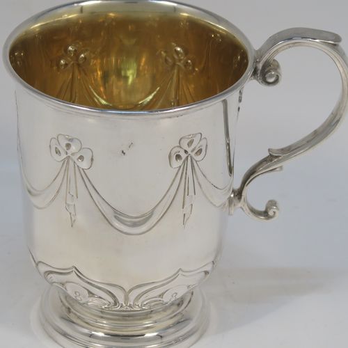 A very pretty Antique Edwardian Sterling Silver christening mug, having a round bellied body, with hand-chased ribbons, swags, and lotus leaf decoration, a cast scroll side-handle, a gold-gilt interior, and sitting on a pedestal foot. This beautiful antique silver christening mug was made by James Dixon and Sons of Sheffield in 1910. The dimensions of this fine hand-made antique silver christening mug are height 10 cms (4 inches), length 10 cms (4 inches), and it weighs approx. 151g (4.9 troy ounces).