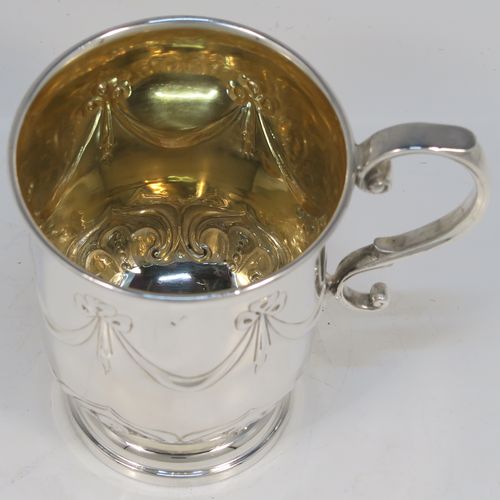 A very pretty Antique Edwardian Sterling Silver christening mug, having a round bellied body, with hand-chased ribbons, swags, and lotus leaf decoration, a cast scroll side-handle, a gold-gilt interior, and sitting on a pedestal foot. This beautiful antique silver christening mug was made by James Dixon and Sons of Sheffield in 1910. The dimensions of this fine hand-made antique silver christening mug are height 10 cms (4 inches), length 10 cms (4 inches), and it weighs approx. 151g (4.9 troy ounces).