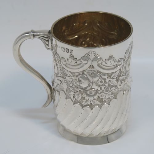 A very pretty Antique Victorian Sterling Silver christening mug, having a round straight-sided body with tucked under belly, all hand-chased with floral, scroll-work, and fluted decoration, a central vacant cartouche, a plain scroll handle, a gold-gilt interior, and all sitting on a collet foot. This beautiful silver mug was made by George Maudsley Jackson of London in 1893. The dimensions of this fine hand-made antique silver christening mug 6.5re height 9.5 cms (3.75 inches), diameter at lip 7 cms (2.6 inches), and it weighs approx. 146g (4.7 troy ounces).   
