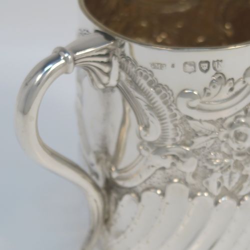 A very pretty Antique Victorian Sterling Silver christening mug, having a round straight-sided body with tucked under belly, all hand-chased with floral, scroll-work, and fluted decoration, a central vacant cartouche, a plain scroll handle, a gold-gilt interior, and all sitting on a collet foot. This beautiful silver mug was made by George Maudsley Jackson of London in 1893. The dimensions of this fine hand-made antique silver christening mug 6.5re height 9.5 cms (3.75 inches), diameter at lip 7 cms (2.6 inches), and it weighs approx. 146g (4.7 troy ounces).   